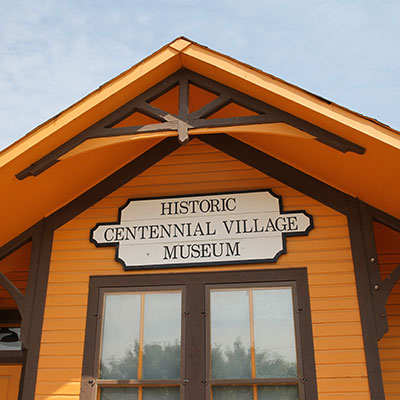 Exterior view of the Historic Centennial Village Museum building and sign in the daytime