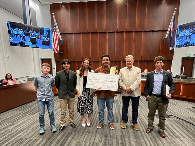 Mayor presents oversized $1,000 scholarship check at a City Council meeting to a young man, a Greeley high school senior that won the 2026 Ed Clark National Youth Service Day Awards.