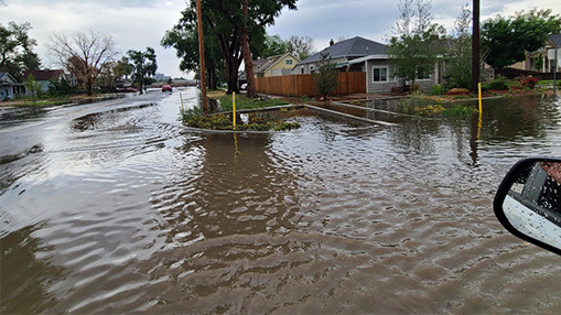 A city street overwhelmed by floodwater after heavy rainfall, impacting homes and traffic.