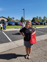 A woman attending a local gathering in a sunny outdoor parking area, holding a vibrant red bag with cars and people in the background.