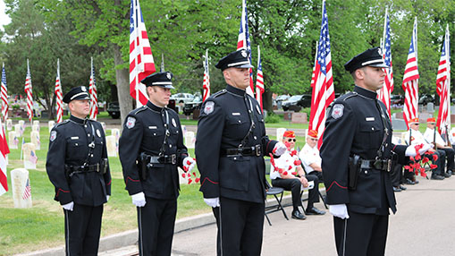 Uniformed officers standing amidst American flags during a solemn commemoration event at Linn Grove Cemetery.