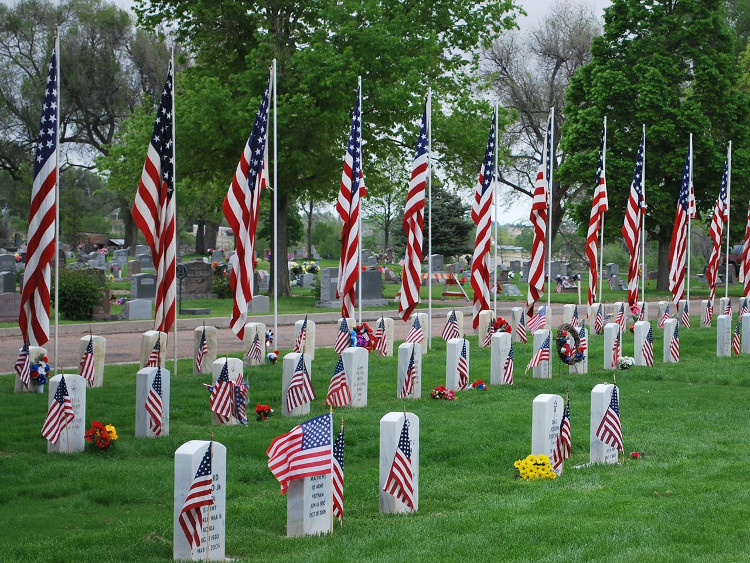 A solemn display of American flags alongside headstones in a cemetery, honoring veterans with memorial decorations.