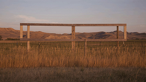 A peaceful scene showcasing a wooden fence surrounded by grassy fields against a backdrop of serene hills and a muted sunset.