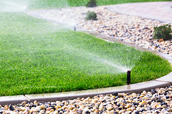 Image showcases a sprinkler system watering a green lawn surrounded by decorative gravel in a residential setting.