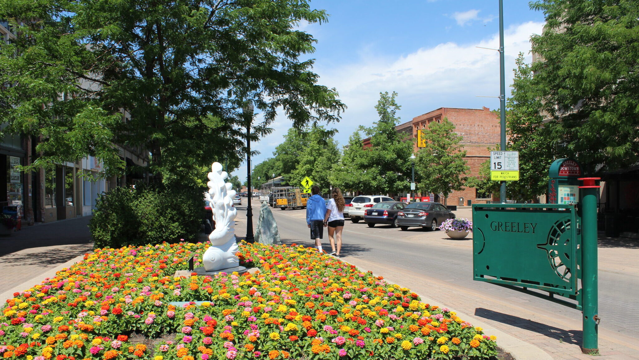 A vibrant view of downtown Greeley, Colorado featuring colorful flowers, bustling streets, and a sunny atmosphere.