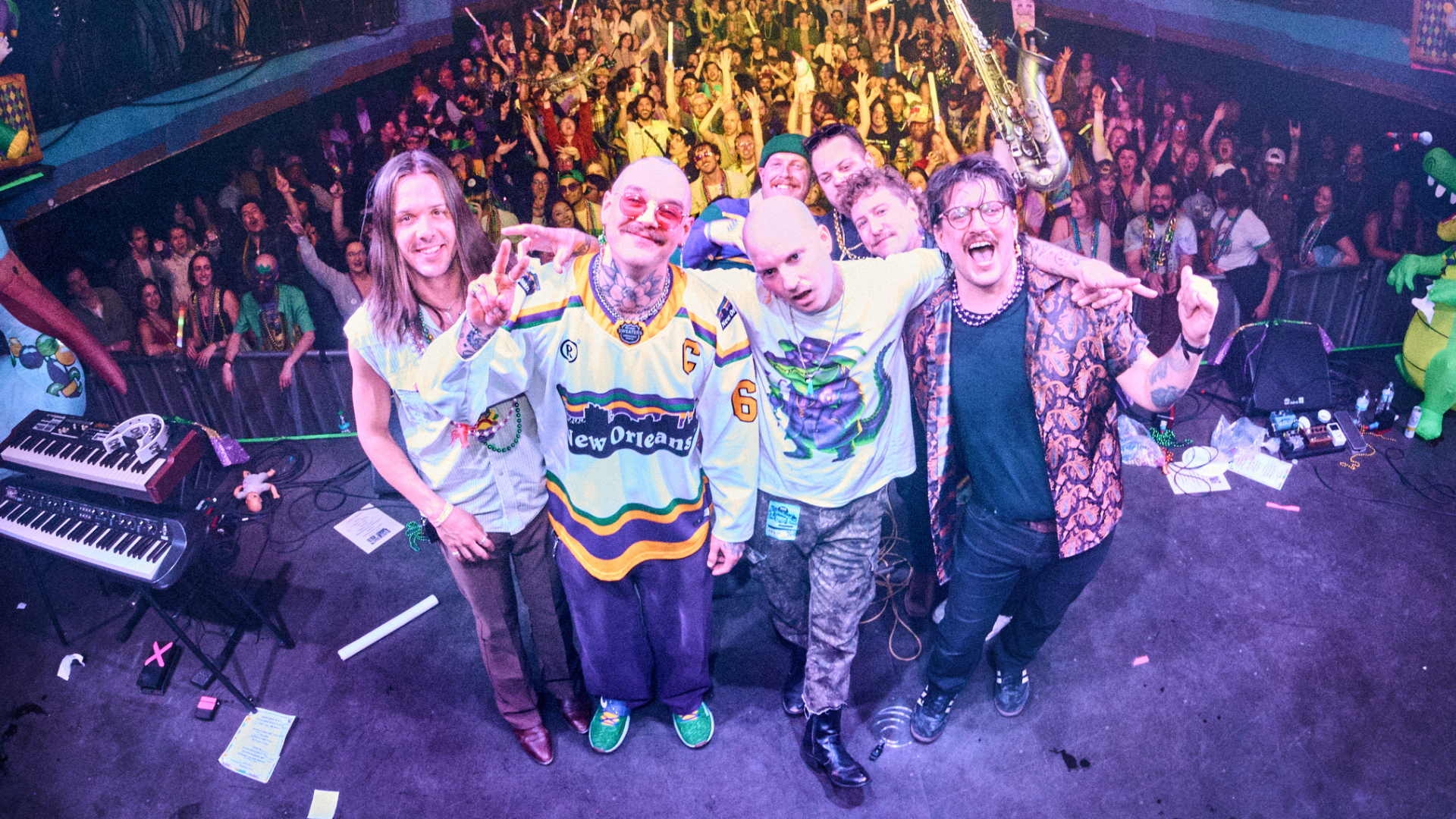 Rootbeer Richie band photo wih four members will play Culture Pop 2026.  Fisheye lens photo of band on stage, with roaring crowd behind them.