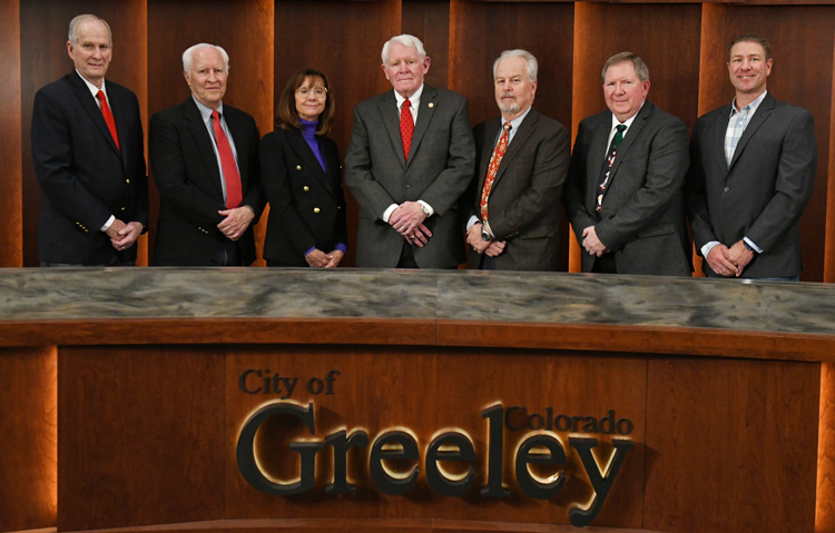 A professional group of individuals standing at a council table during a board meeting in Greeley, Colorado.