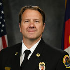 Professional image of a fire department official dressed in uniform with a flag background.
