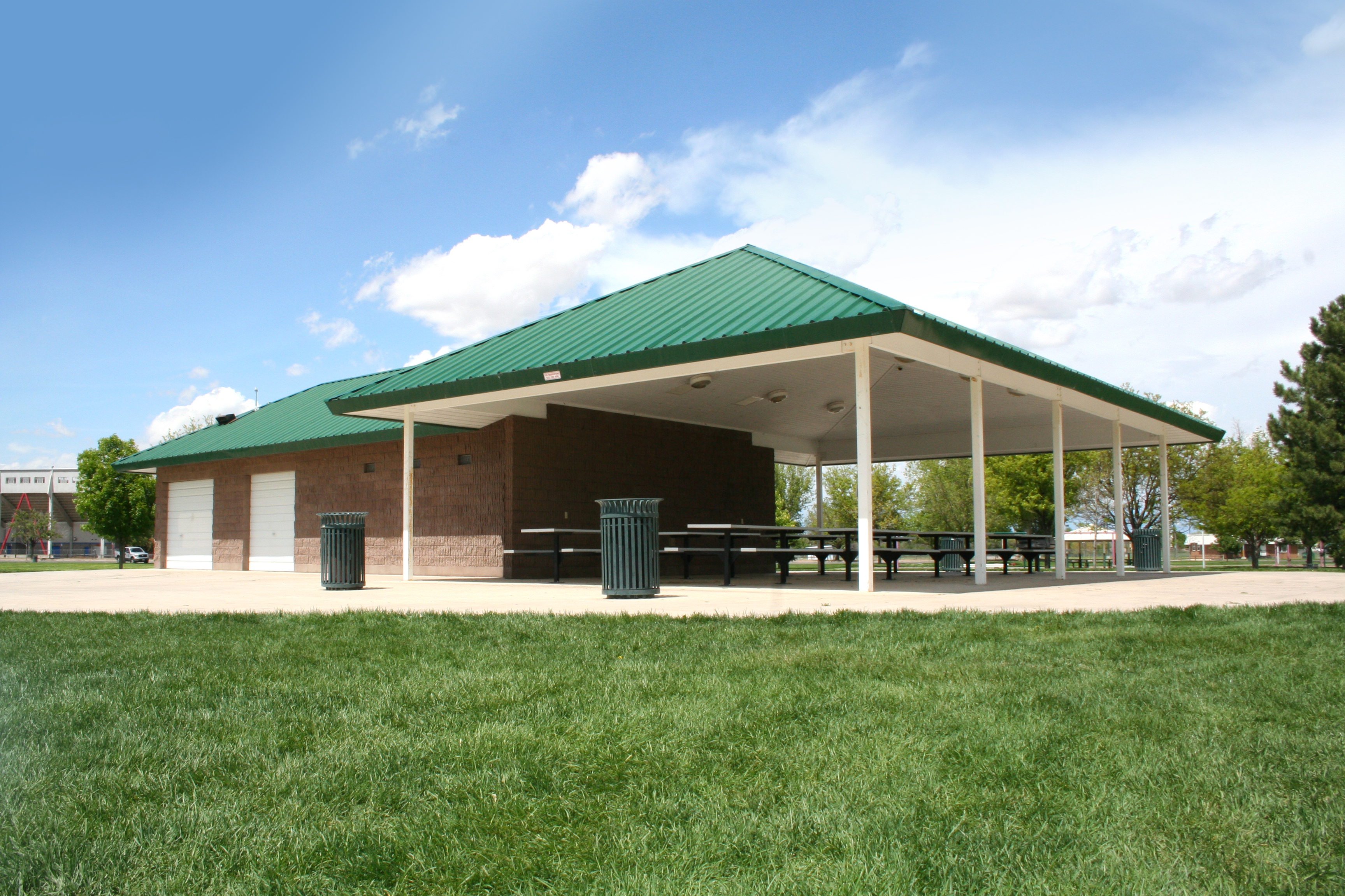 Exterior of the Platte River Pavilion, featuring fixed picnic bench tables, steel waste receptacles, and a beautiful park setting
