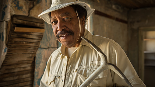 A person holding a tool in a worn-down rural structure, indicative of renovation or preservation efforts.
