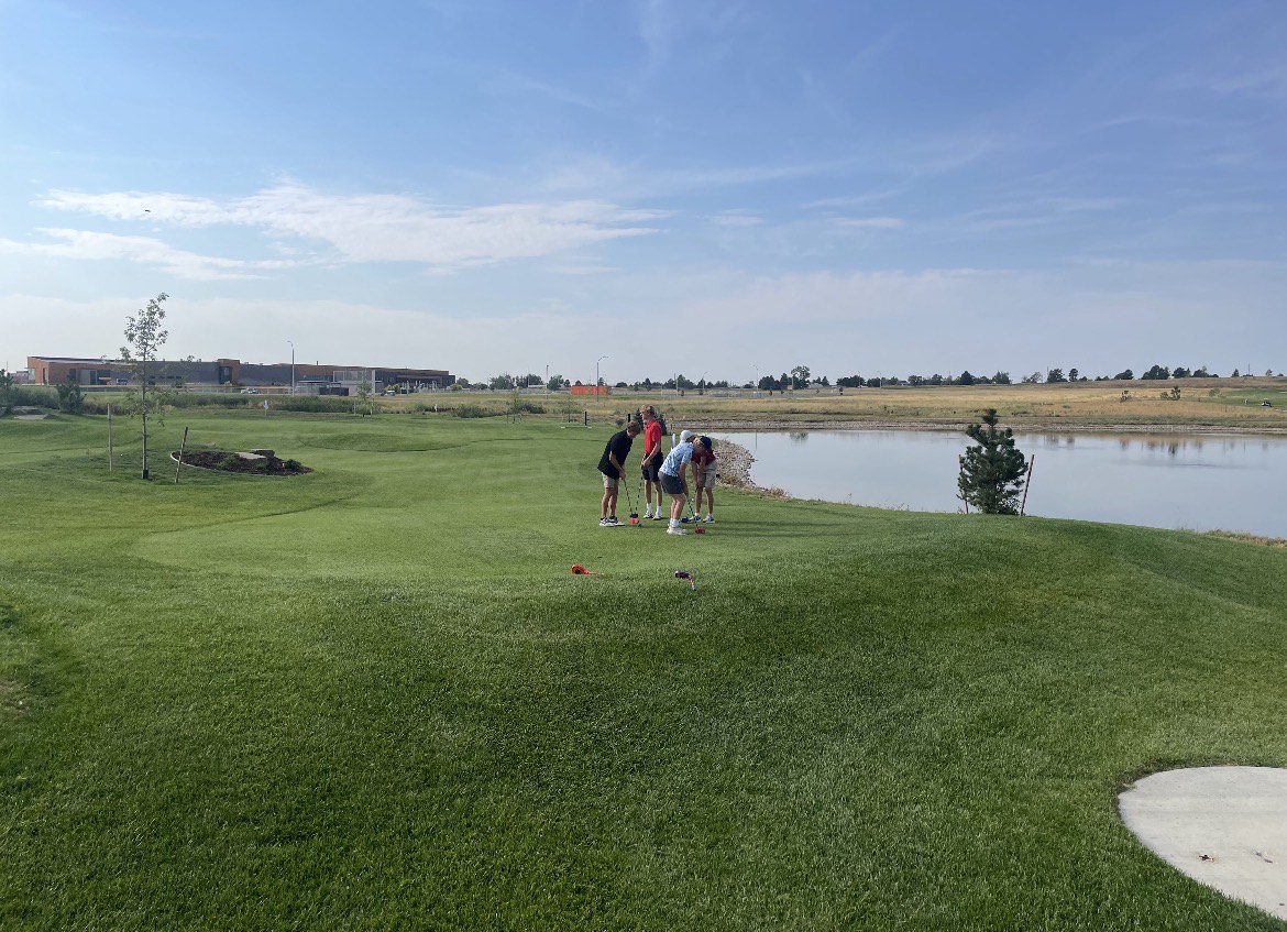 Group of golfers preparing to putt on the short course at Boomerang Links with a pond and open landscape in the background
