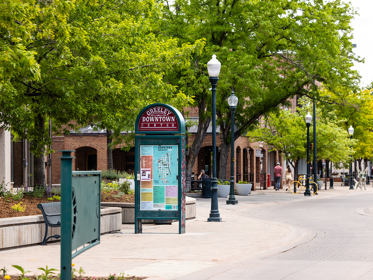 Street view of downtown Greeley showing storefronts and a Greeley Downtown directory