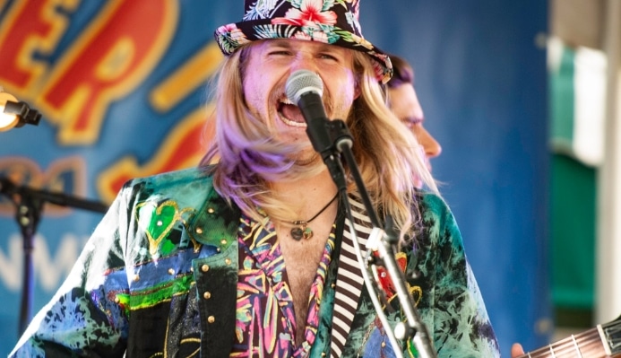 A musician passionately singing and playing guitar during the vibrant atmosphere of the Greeley Blues Jam event.