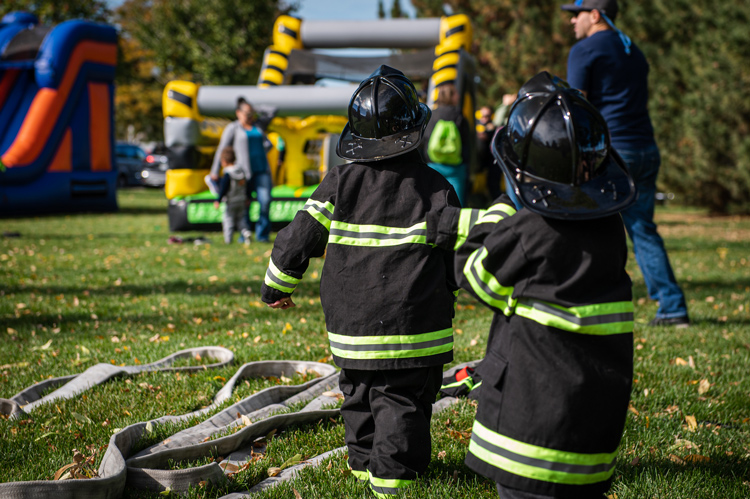 Children enjoying activities dressed in firefighter uniforms during a community event.