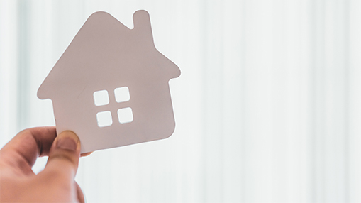 A hand holding a paper cutout of a house, symbolizing community housing and residential initiatives.