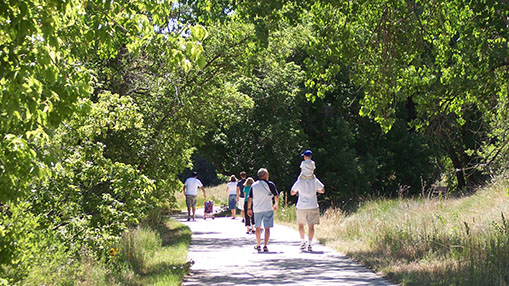 Residents walking and exploring Greeley's scenic trail surrounded by lush greenery.
