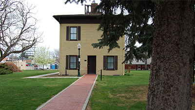 A historic two-story building surrounded by green lawns and trees, showcasing the cultural heritage of Greeley.