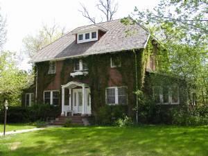 A historic brick house surrounded by green trees and ivy, showcasing early 20th-century design.