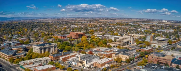Aerial view, looking northwest, of downtown Greeley. Buildings, trees, mountains, and sky are shown in the image.