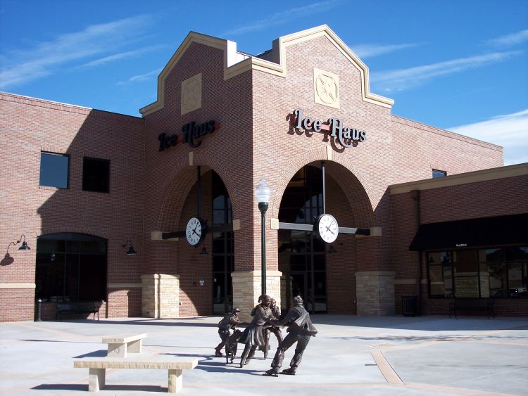 The modern brick exterior of the Greeley Ice Haus facility in Greeley, Colorado, featuring a sculpture of children playing in front.