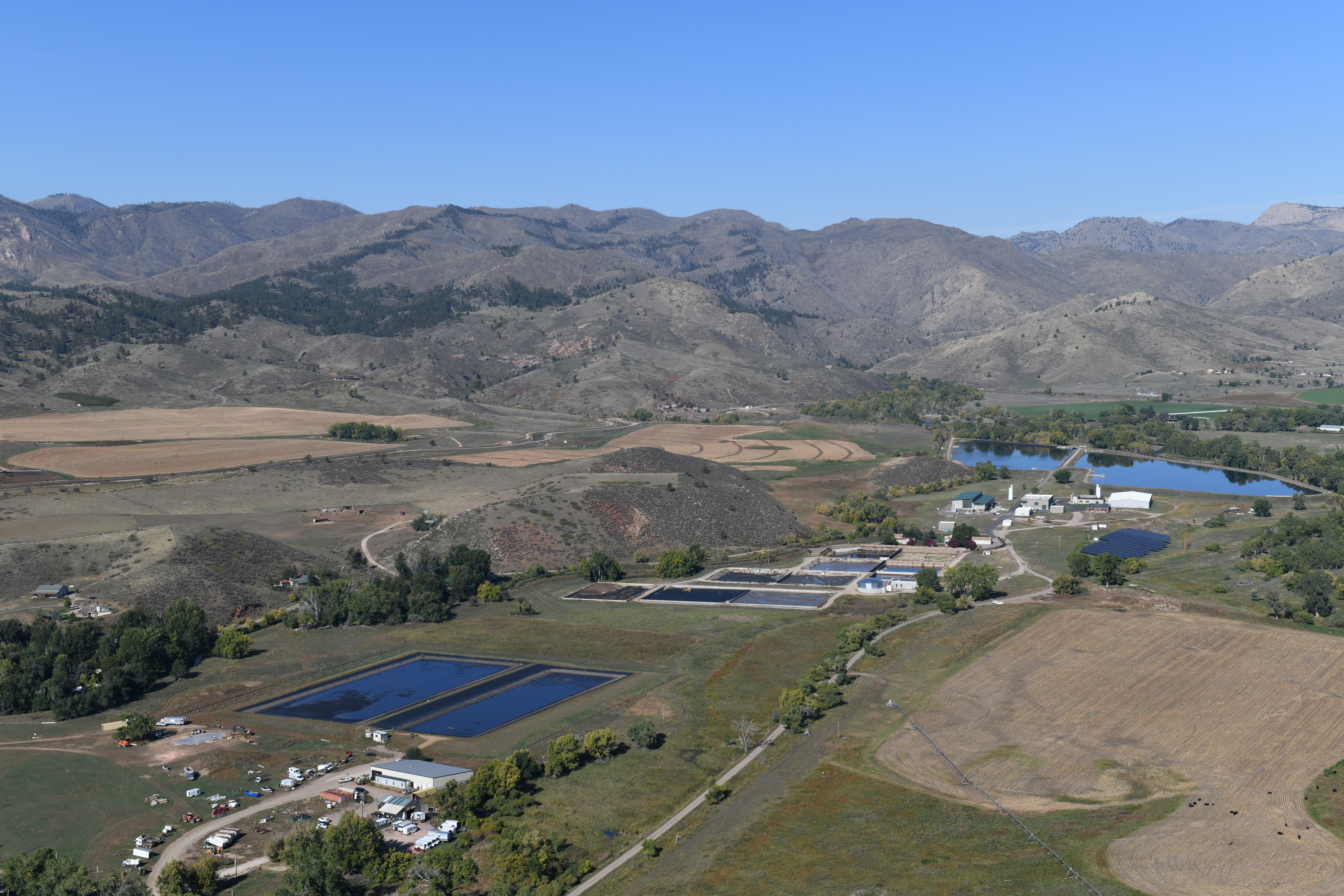 Aerial photograph of Bellvue Drinking Water Treatment Plant during the summer. Image shows water treatment facility buildings, raw ponds, drying ponds, and mountains in the background.