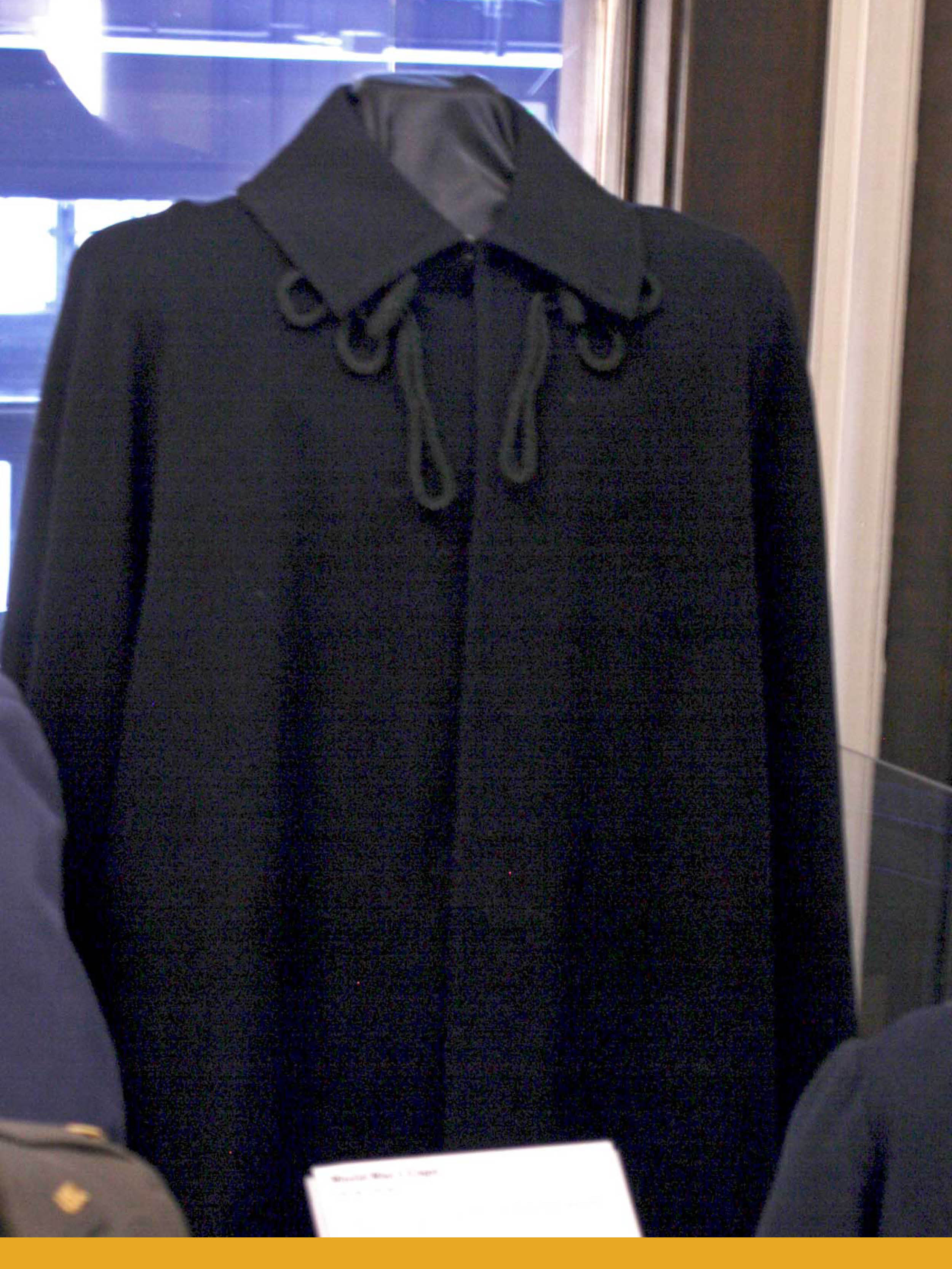 A mannequin wearing a dark blue wool cape with a collar and black decorative cords under the collar