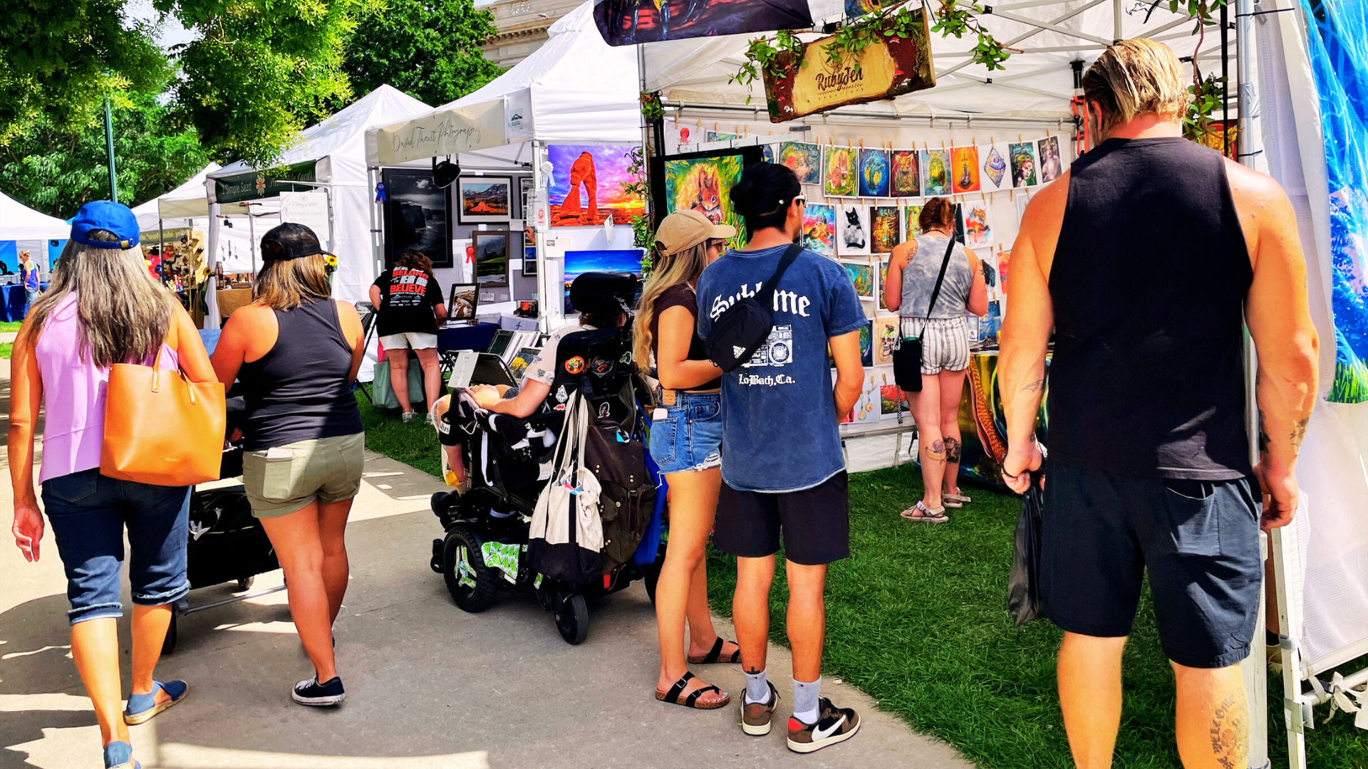 Crowd of people down a busy sidewalk of artist booths at the Greeley Arts Picnic.   