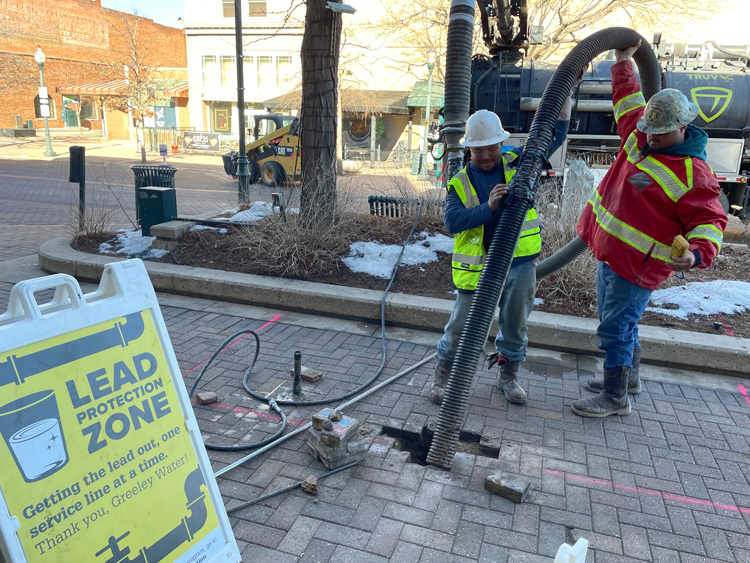 Workers operating equipment during a lead pipe replacement project in downtown Greeley.