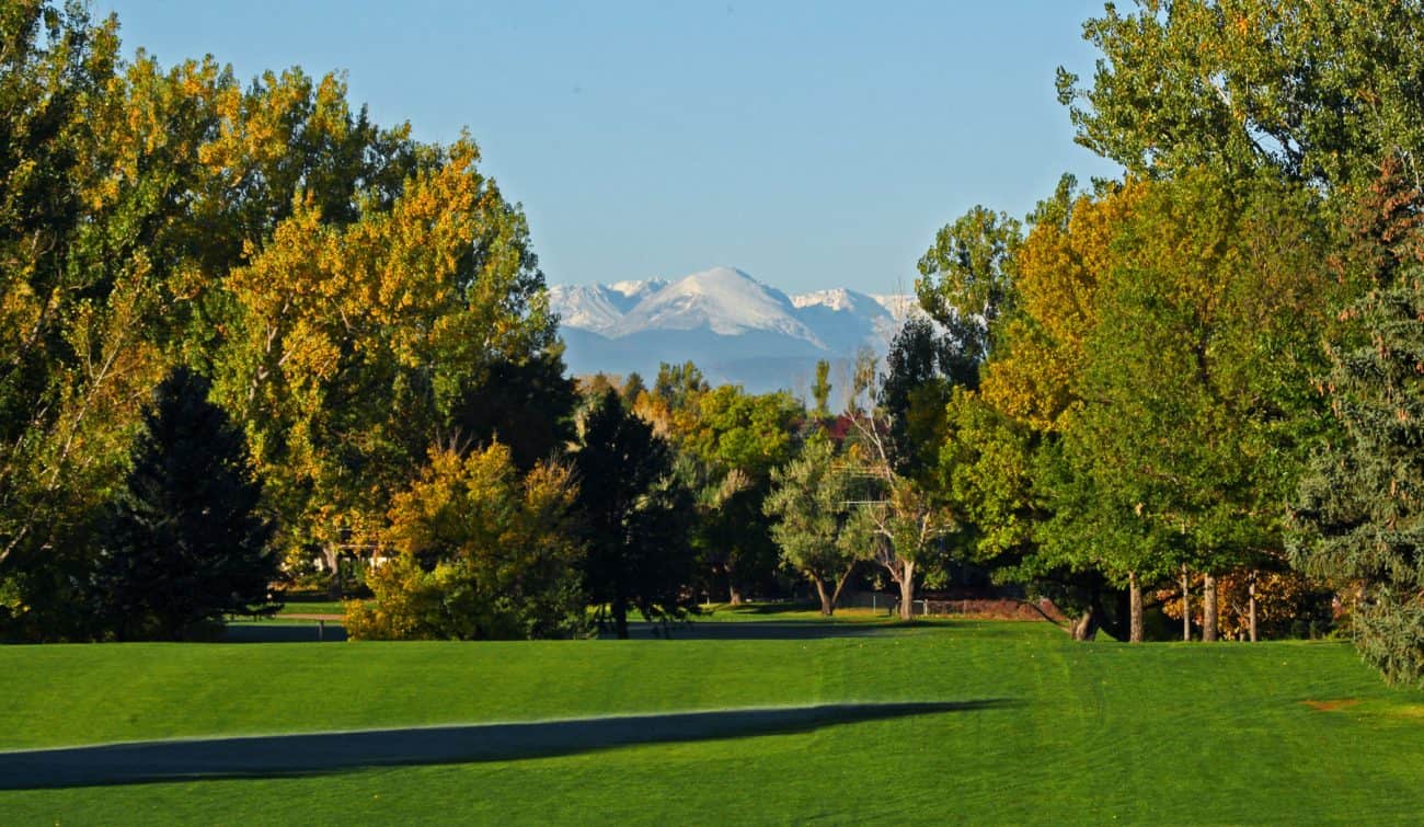 A picturesque view of a golf course surrounded by greenery and snow-capped mountains in the distance.