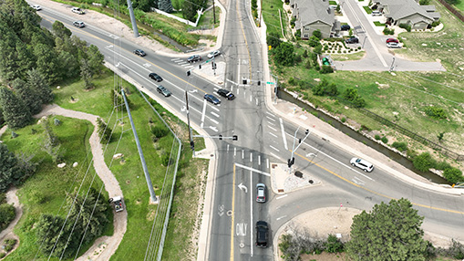 An aerial view of a multi-lane intersection showing both urban and suburban surroundings, with traffic flow and nearby greenery.