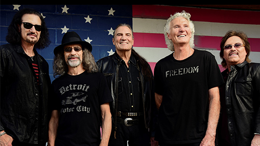 Band members posing in front of an American flag backdrop, showcasing unity and a patriotic theme.