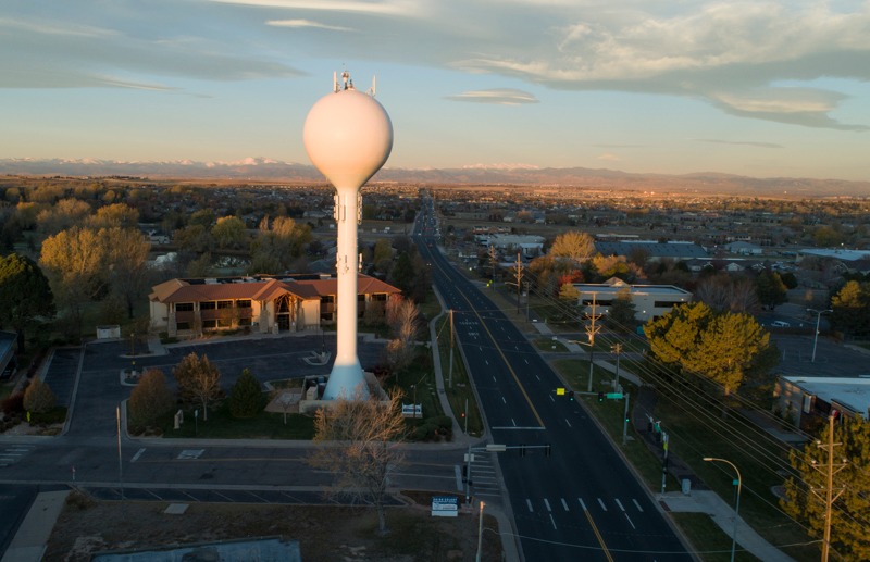 This image depicts a large white water tower at the corner of a T-intersection in Greeley.  