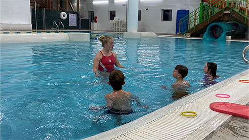 A swimming instructor teaches children inside a public indoor pool facility.