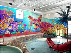 A vibrant indoor pool area featuring colorful marine murals and recreational slides.