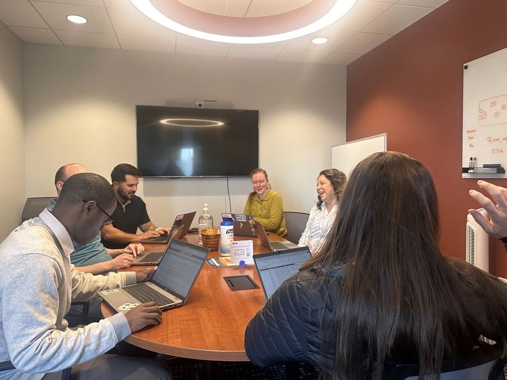 Budget Team sitting around conference table, working on laptops, talking and laughing