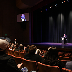 Mayor John Gates delivering the State of the City address to an audience in a theater setting.