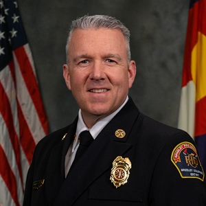 Professional portrait of Chief Brian Kuznik in uniform with flags in the background.