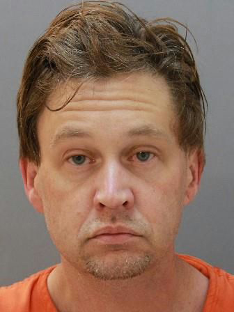 A close-up, front-facing portrait of a man with light skin, blue eyes, and medium-short brown hair. He is looking directly at the camera with a neutral expression. The image is framed by a solid blue border on the left and right sides.