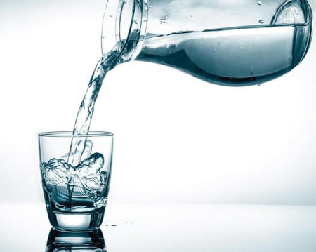 A close-up view of fresh water being poured from a glass pitcher into a transparent glass on a clean surface.
