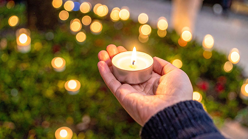 A hand holding a candle at a vigil with other candle lights shining in the background