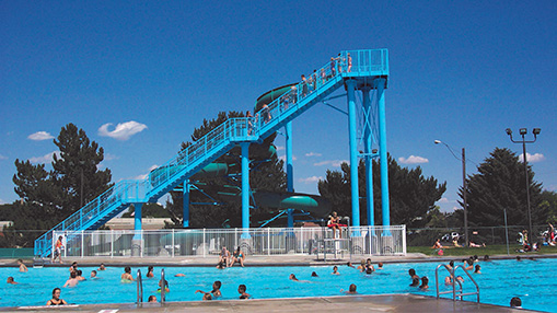 Outdoor swimming pool featuring a large blue slide surrounded by residents enjoying activities.