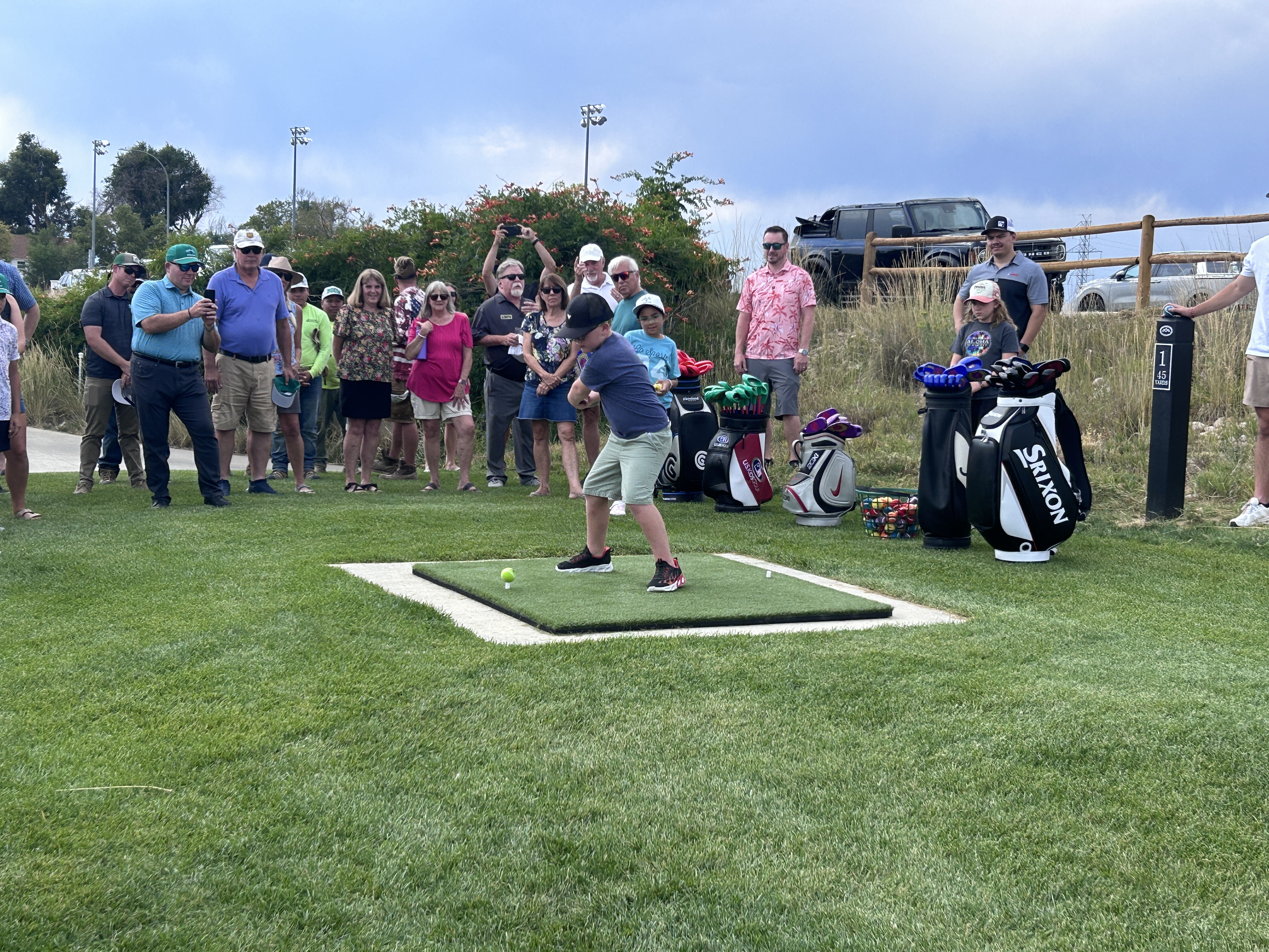 Participant hitting a ceremonial tee shot at the opening ceremony of the Mike Lee 9 at Boomerang Links with spectators watching.