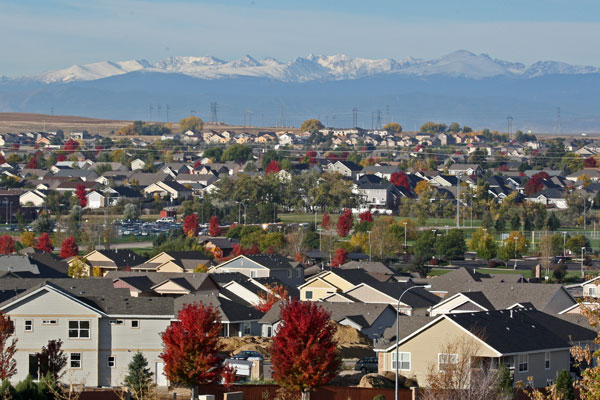 A picturesque view of suburban Greeley, Colorado, showcasing colorful houses, autumn foliage, and the distant Rocky Mountains.